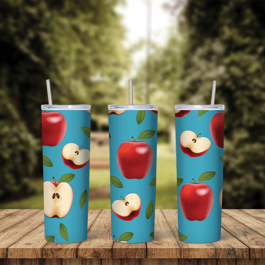 An apple tumbler wrap with red apples, apple halves showing seeds and green leaves scattered over a bright blue background. Sublimation design