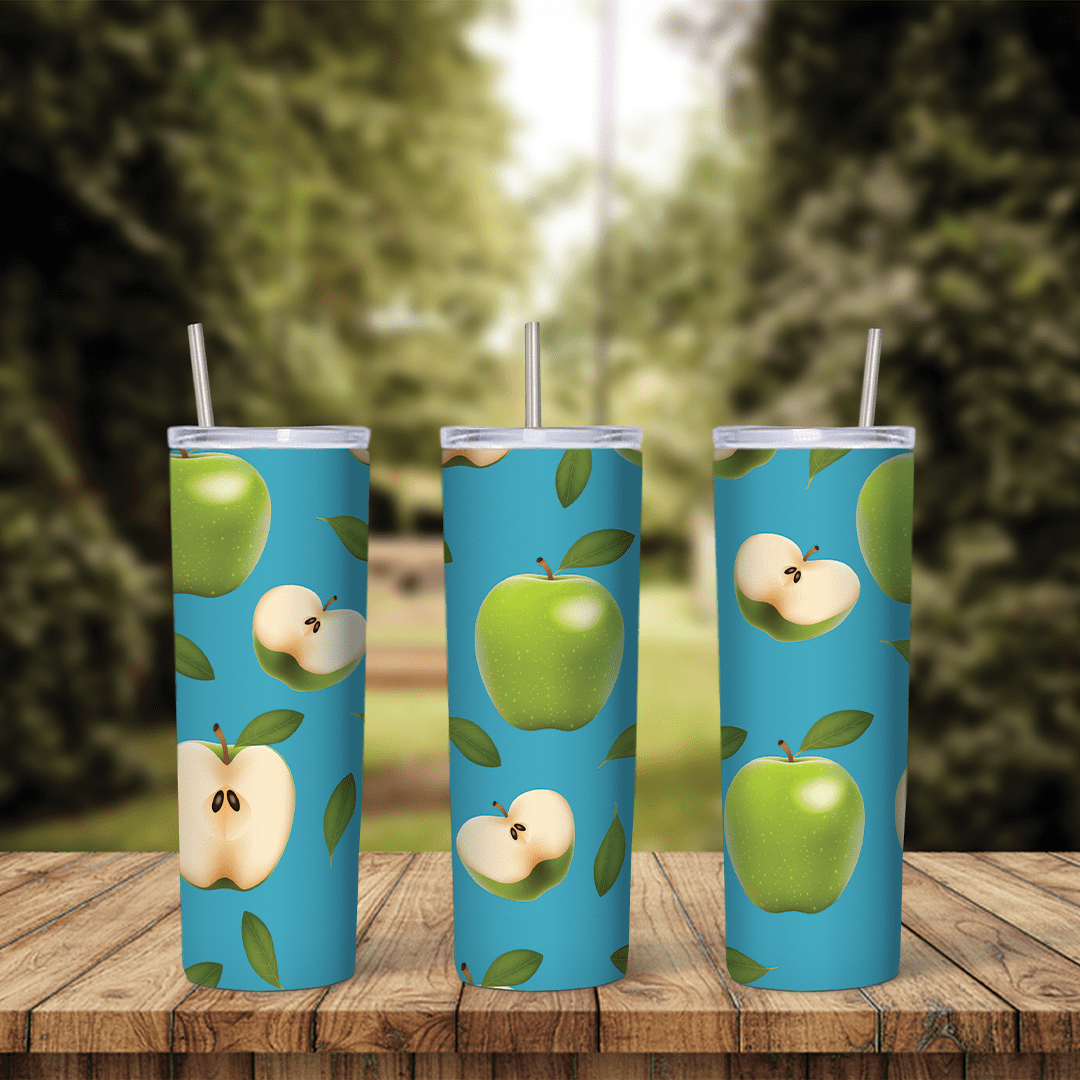 An apple tumbler wrap with green apples, apple halves showing seeds and green leaves scattered over a bright blue background. Sublimation design
