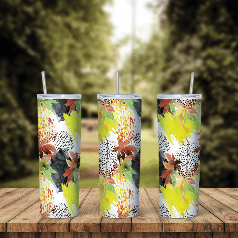 A full 20 oz skinny tumbler wrap with yellow, green and brown autumn leaves, black brush strokes and dotted patches on white. Sublimation design